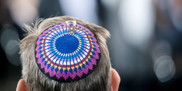 Ein Mann hält sich seine Kippa mit einem blauen Davidstern auf dem Kopf, daneben weitere Männer mit Kippot Ein Mann hält sich seine Kippa mit einem blauen Davidstern auf dem Kopf, daneben weitere Männer mit Kippot