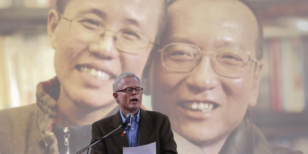 Ian Johnson hält eine Rede für Liu Xiaobo - vorne ein Mann mit einem Zettel, hinten an die Wand projiziert ein Mann und eine Frau - Liu Xia und Liu Xiaobo Ian Johnson hält eine Rede für Liu Xiaobo - vorne ein Mann mit einem Zettel, hinten an die Wand projiziert ein Mann und eine Frau - Liu Xia und Liu Xiaobo