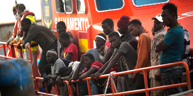 Menschen stehen an der Reling eines orangefarbenen Schiffes Menschen stehen an der Reling eines orangefarbenen Schiffes