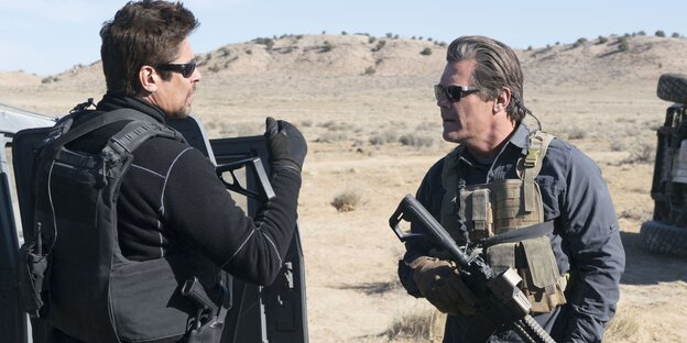 Benicio del Toro und Josh Brolin stehen in der Wüste und tragen schusssichere Westen und Waffen Benicio del Toro und Josh Brolin stehen in der Wüste und tragen schusssichere Westen und Waffen