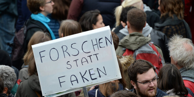 Ein Demonstrant hält ein Pappschild hoch mit der Inschrift "Forschen statt Faken"rotes gegen Ein Demonstrant hält ein Pappschild hoch mit der Inschrift "Forschen statt Faken"rotes gegen