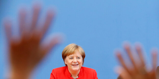 Angela Merkel lächelt, vor ihr heben sich Hände Angela Merkel lächelt, vor ihr heben sich Hände