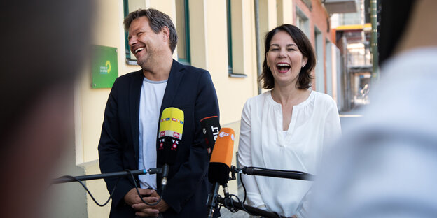 Habeck und Baerbock stehen lachend nebeneinander vor Mikrofonen Habeck und Baerbock stehen lachend nebeneinander vor Mikrofonen