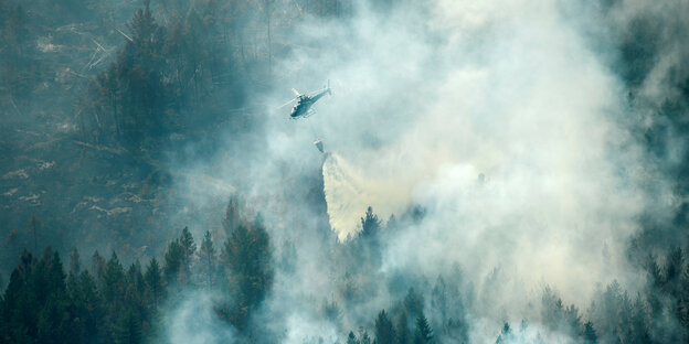 Eine Hubschrauber mit Löschwasser fliegt über einen brennenden Wald Eine Hubschrauber mit Löschwasser fliegt über einen brennenden Wald
