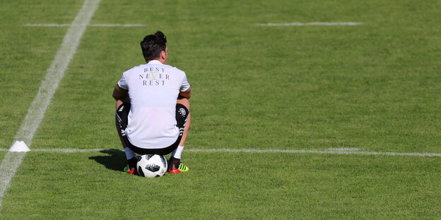 Mesut Özl sitzt auf einem Fußballplatz auf einem Ball, er ist von hinten zu sehen Mesut Özl sitzt auf einem Fußballplatz auf einem Ball, er ist von hinten zu sehen