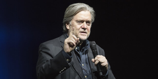 Steve Bannon hält ein Mikro in der einen Hand und streckt die andere mahnend mit erhobenem Zeigefinger hoch Steve Bannon hält ein Mikro in der einen Hand und streckt die andere mahnend mit erhobenem Zeigefinger hoch