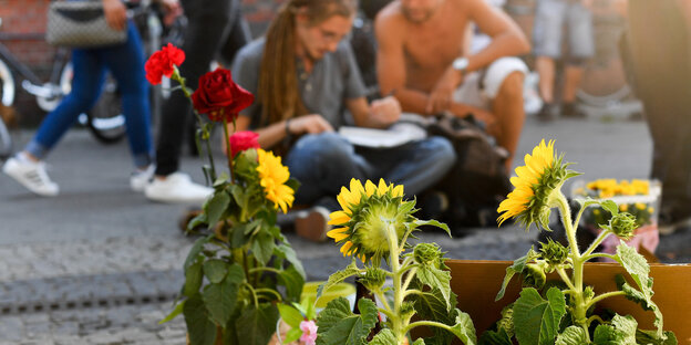 Blumen im Vordergrund, dahinter sitzen Menschen auf der Straße Blumen im Vordergrund, dahinter sitzen Menschen auf der Straße