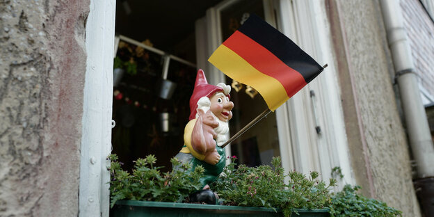 Ein Gartenzweg, der eine Deutschlandfahne schwenkt, steht in einem Blumenkasten Ein Gartenzweg, der eine Deutschlandfahne schwenkt, steht in einem Blumenkasten