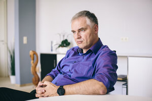 Jörg Röglin mit einem lilafarbenen Hemd am Tisch sitzend Jörg Röglin mit einem lilafarbenen Hemd am Tisch sitzend