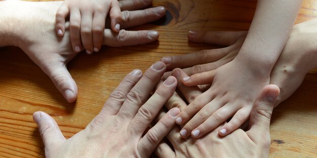 Berührende Hände auf einem Tisch: zwei Erwachsene und ein Kind Berührende Hände auf einem Tisch: zwei Erwachsene und ein Kind
