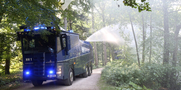 Ein Wasserwerfer fährt durch einen Park und spritzt Wasser in Bäume und Büsche Ein Wasserwerfer fährt durch einen Park und spritzt Wasser in Bäume und Büsche
