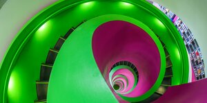 Treppenhaus von oben fotografiert. Es leuchtet in den Farben grün und lila