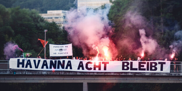 Menschen auf einer Brücke mit Pyro-Feuerwerk und Transparent mit der Aufschrift "Havanna Acht bleibt" Menschen auf einer Brücke mit Pyro-Feuerwerk und Transparent mit der Aufschrift "Havanna Acht bleibt"