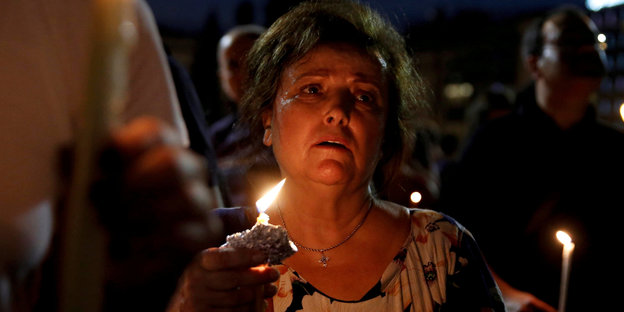 Eine Frau hält bei einer Trauerfeier für die 91 Toten nach Waldbränden in Athen eine Kerze