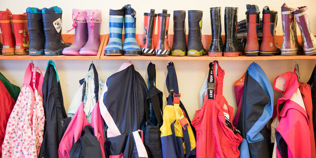 Kita: Gummistiefel nebeneinander auf einem Bord, darunter hängen Jacken Kita: Gummistiefel nebeneinander auf einem Bord, darunter hängen Jacken
