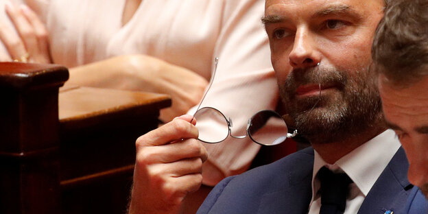 Edouard Philippe sitzt zwischen anderen Parlamentariern. Er hat sich die Brille abgesetzt und hält diese vor seinem Gesicht Edouard Philippe sitzt zwischen anderen Parlamentariern. Er hat sich die Brille abgesetzt und hält diese vor seinem Gesicht