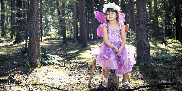 Ein Kind im rosa Feenkostüm sitzt auf einem Hocker im Wald Ein Kind im rosa Feenkostüm sitzt auf einem Hocker im Wald