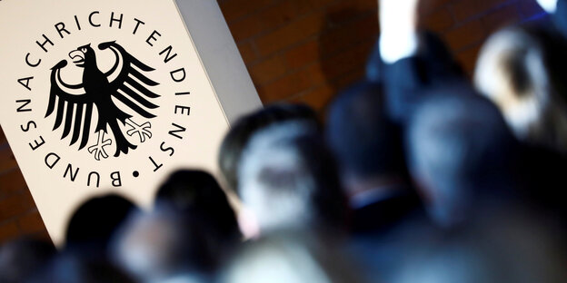 Erleuchtetes BND-Logo an einer Wand, davor viele Köpfe von hinten aufgenommen Erleuchtetes BND-Logo an einer Wand, davor viele Köpfe von hinten aufgenommen