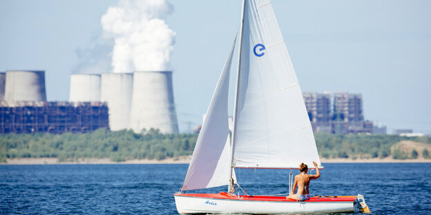 Eine junge Frau winkt auf dem Bärwalder See gegenüber dem Kohlekraftwerk Boxberg aus einem Segelboot. Eine junge Frau winkt auf dem Bärwalder See gegenüber dem Kohlekraftwerk Boxberg aus einem Segelboot.