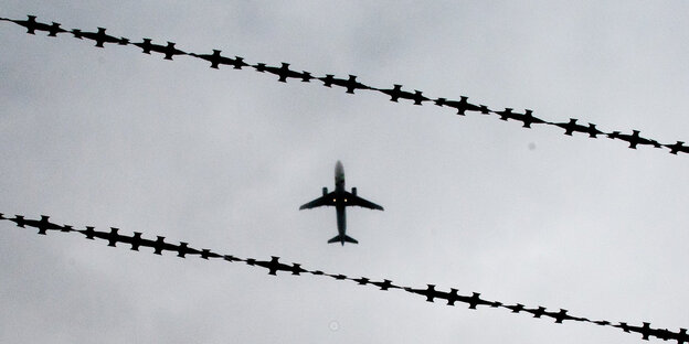 Ein Flugzeug fliegt über Stacheldraht am Himmel Ein Flugzeug fliegt über Stacheldraht am Himmel