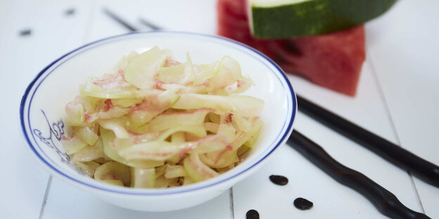 Ein Salat auf einem weißen Teller, daneben Stäbchen und Wassermelone Ein Salat auf einem weißen Teller, daneben Stäbchen und Wassermelone
