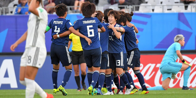 Im Hintergrund jubeln japanische Fußballerinnen, im Vordergrund geht eine traurige deutsche Spielerin Im Hintergrund jubeln japanische Fußballerinnen, im Vordergrund geht eine traurige deutsche Spielerin