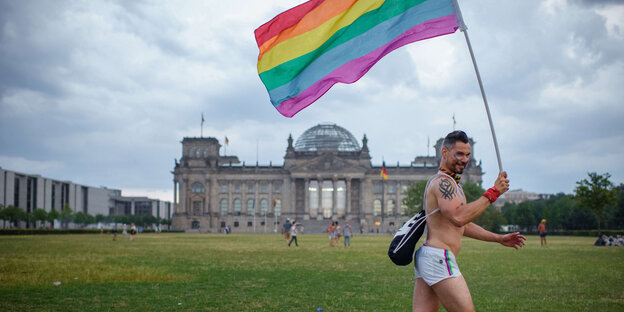 Ein Mann rennt mit Regenbogenflagge am Reichstag vorbei. Ein Mann rennt mit Regenbogenflagge am Reichstag vorbei.