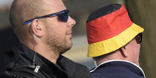 Mann mit Sonnenbrille und Headset neben Mann mit schwarz-rot-goldenem Hut Mann mit Sonnenbrille und Headset neben Mann mit schwarz-rot-goldenem Hut