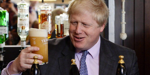 Boris Johnson hält ein Glas Bier in die Luft und grinst es an Boris Johnson hält ein Glas Bier in die Luft und grinst es an