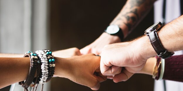 Vier Menschen geben sich die Faust und tragen Armbanduhren Vier Menschen geben sich die Faust und tragen Armbanduhren
