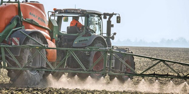 Ein Traktor fährt über einen Acker und versprüht hinter sich eine Flüssigkeit