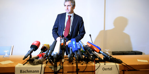 Frank Richter steht vor vielen Mikros und zwei Namenschildern, auf denen „Bachmann“ und „Oertel“ steht Frank Richter steht vor vielen Mikros und zwei Namenschildern, auf denen „Bachmann“ und „Oertel“ steht