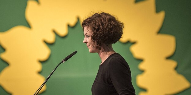 Gesine Agena ist im Profil zu sehen, sie steht an einem Rednerpult vor dem Sonnenblumen-Logo der Grünen Gesine Agena ist im Profil zu sehen, sie steht an einem Rednerpult vor dem Sonnenblumen-Logo der Grünen