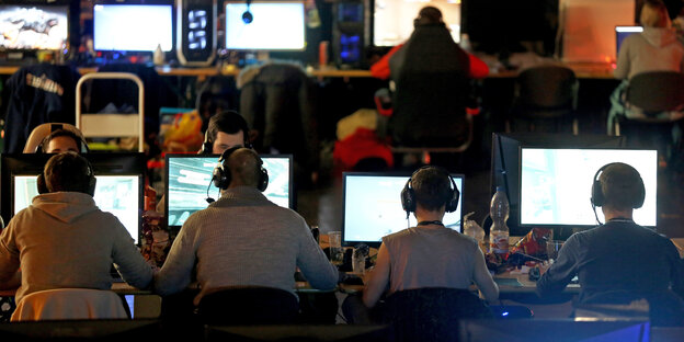 Computerspieler*innen sitzen hinter Monitoren. Computerspieler*innen sitzen hinter Monitoren.