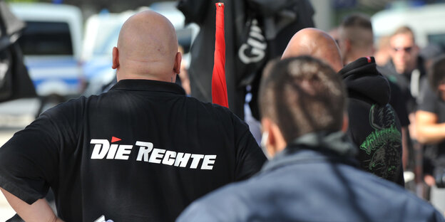 Ein glatzköpfiger Mann mit einem schwarzen T-Shirt, auf dem das Logo der Partei "Die Rechte" abgebildet ist. Ein glatzköpfiger Mann mit einem schwarzen T-Shirt, auf dem das Logo der Partei "Die Rechte" abgebildet ist.