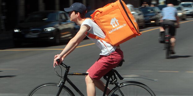 Lieferando-Radler mit orangem Rucksack unterwegs Lieferando-Radler mit orangem Rucksack unterwegs