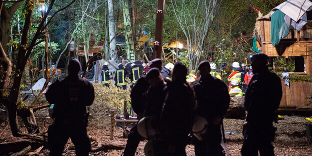 Polizisten und Feuerwehrmänner stehen im Hambacher Forst und versuchen Aktivisten aus einem komplizierten Tunnelsystem zu holen.