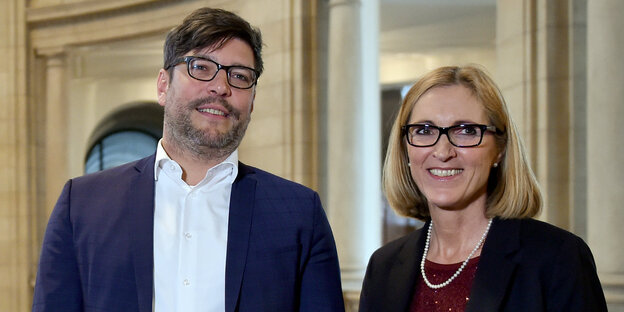 Ein Mann und eine Frau stehen nebeneinander und lächeln in die Kamera Ein Mann und eine Frau stehen nebeneinander und lächeln in die Kamera