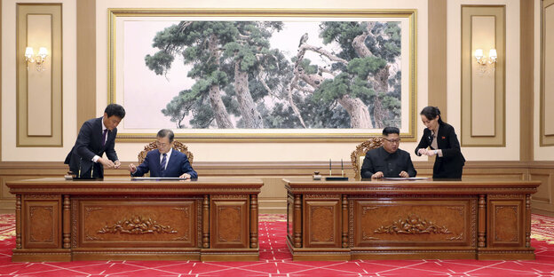 Zwei Männer, Moon Jae In und Kim Jong Un, sitzen an zwei unterschiedlichen Tischen, die nebeneinander stehen. Sie unterschreiben etwas Zwei Männer, Moon Jae In und Kim Jong Un, sitzen an zwei unterschiedlichen Tischen, die nebeneinander stehen. Sie unterschreiben etwas