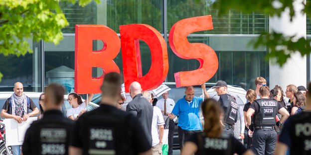 AkstistInnen halten riesige Buchstaben "BDS" hoch, davor stehen PolizistInnen AkstistInnen halten riesige Buchstaben "BDS" hoch, davor stehen PolizistInnen