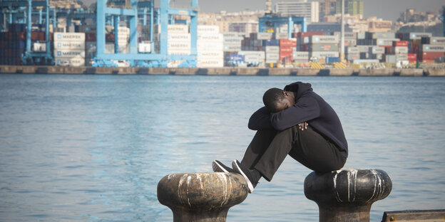 Ein Migrant sitzt am Hafen von Algeciras in Südspanien und hat den Kopf auf die Knie gelegt Ein Migrant sitzt am Hafen von Algeciras in Südspanien und hat den Kopf auf die Knie gelegt