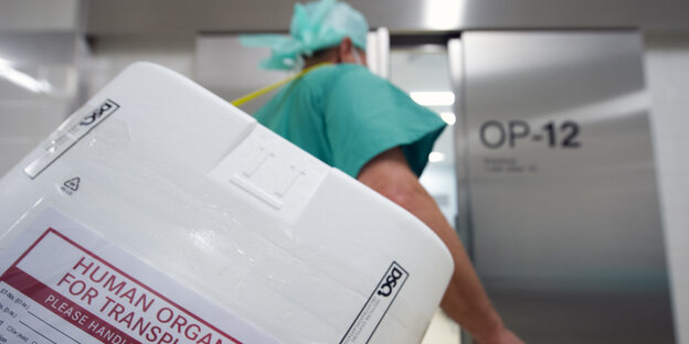 Ein Mann in grüner OP-Kleidung trägt einen Styropor-Behälter zum Transport von Organen Ein Mann in grüner OP-Kleidung trägt einen Styropor-Behälter zum Transport von Organen