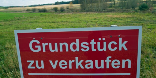 Ein Bauschild auf grüner Wiese mit dem Spruch: Grundstück zu verkaufen