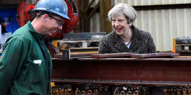 In Großbritannien lacht Theresa May mit einem Stahlarbeiter In Großbritannien lacht Theresa May mit einem Stahlarbeiter