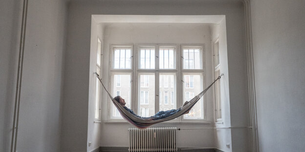Ein leeres Zimmer, am Fenster eine Hängematte, darin liegt ein Mann Ein leeres Zimmer, am Fenster eine Hängematte, darin liegt ein Mann