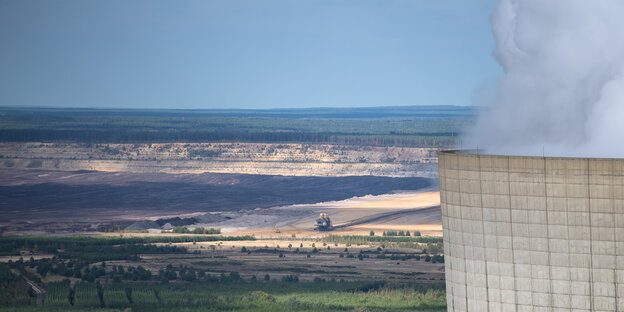 Ein Kühlturm vor einer Landschaft mit Braunkohletagebau