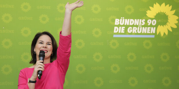 Annalena Baerbock winkt und spricht in ein Mikro, hinter ihr das Logo der Grünen Annalena Baerbock winkt und spricht in ein Mikro, hinter ihr das Logo der Grünen