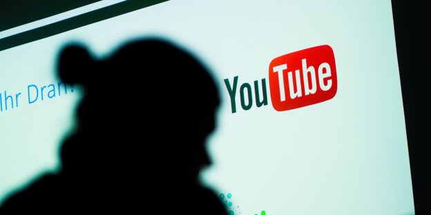 Das Foto zeigt einen Schatten vor einem Logo von YouTube Das Foto zeigt einen Schatten vor einem Logo von YouTube