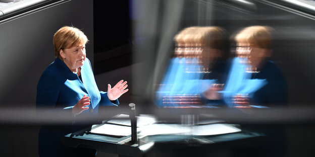Angela Merkel steht im Plenum des Deutschen Bundestags und hebt beide Hände Angela Merkel steht im Plenum des Deutschen Bundestags und hebt beide Hände