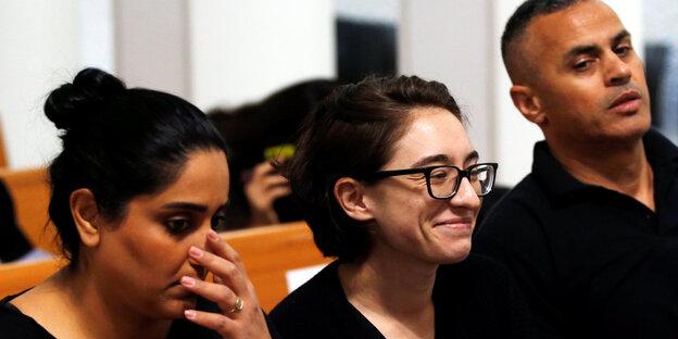 Ein Frau sitzt in einem Gerichtssaal, rechts und links jeweils eine BeamtIn Ein Frau sitzt in einem Gerichtssaal, rechts und links jeweils eine BeamtIn